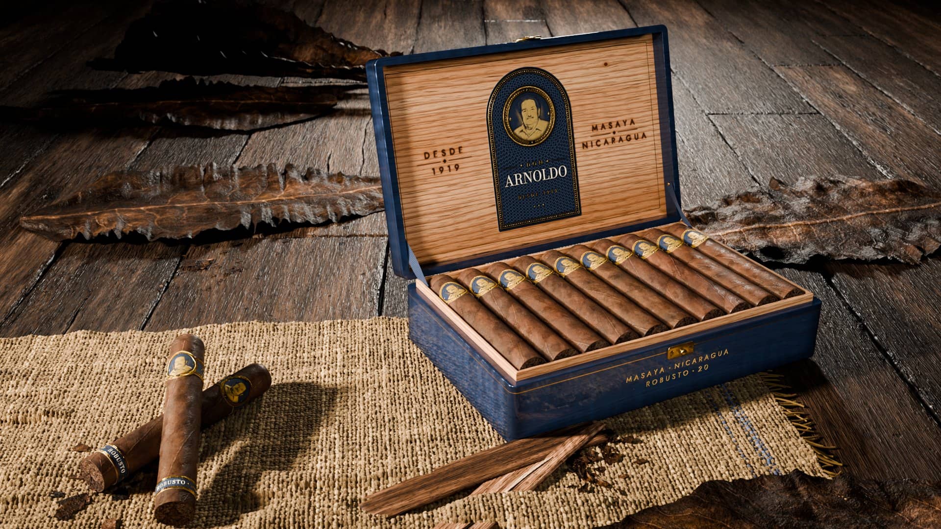 La caja azul de Don Arnoldo abierta, con los puros en su camada y la etiqueta en el interior de cedro; delante, dos puros sueltos sobre yute.