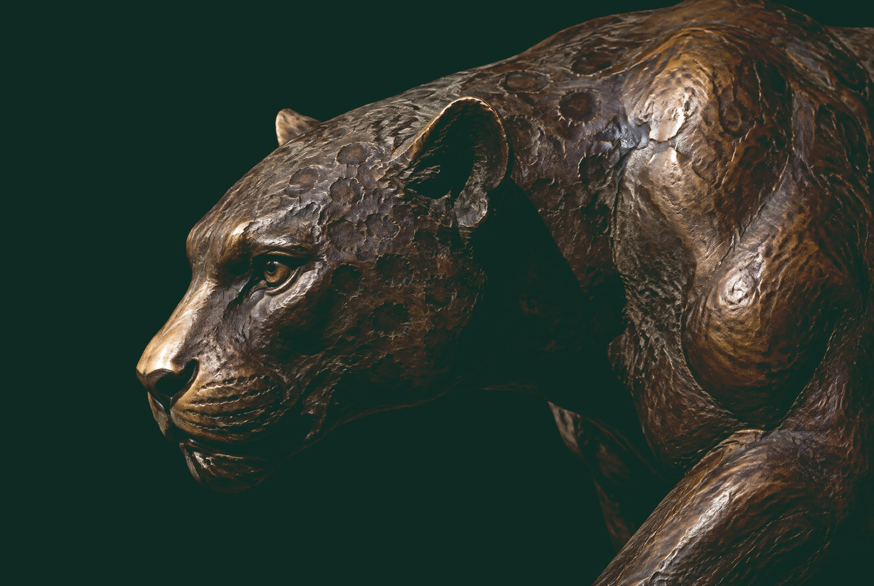 Escultura de bronce de un jaguar al acecho, de perfil, con la cabeza baja y la mirada fija al frente.